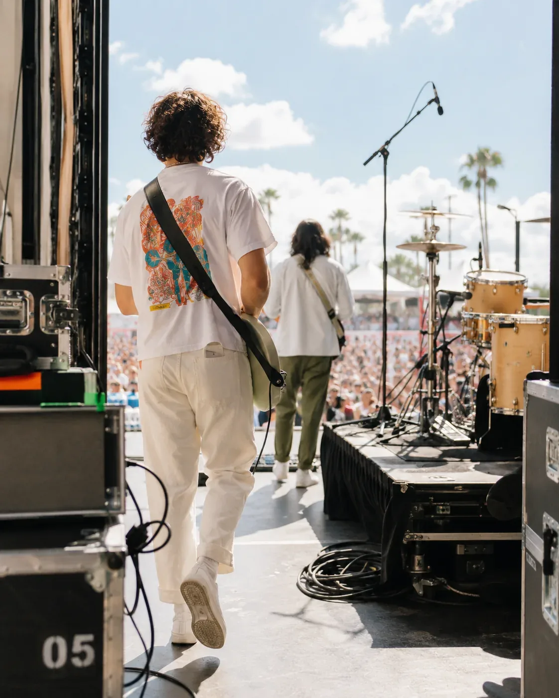 A guitarist walking onto an outdoor live stage with a band and audience ahead